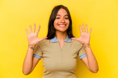 Sarı arka planda izole edilmiş genç İspanyol kadın on numarayı elleriyle gösteriyor..