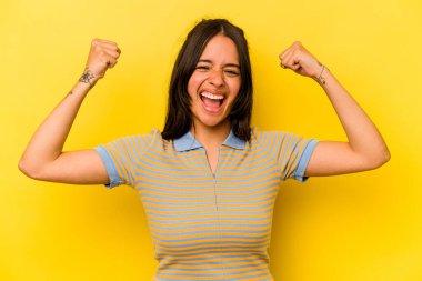 Sarı arka planda izole edilmiş genç İspanyol kadın güçlü hareketlerini kollarıyla gösteriyor, kadın gücünün sembolü.
