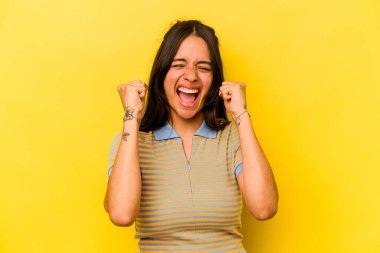 Sarı arka planda izole edilmiş genç İspanyol kadın tasasız ve heyecanlı bir şekilde tezahürat yapıyor. Zafer konsepti.