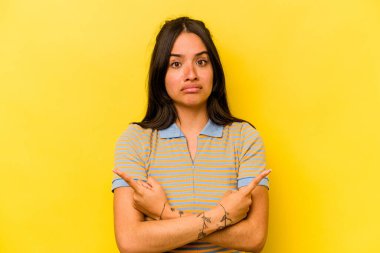 Sarı arka plan noktalarında izole edilmiş genç İspanyol kadın iki seçenek arasında seçim yapmaya çalışıyor..