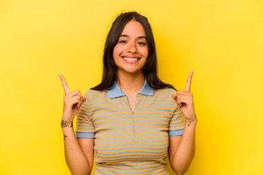 Sarı arka planda izole edilmiş genç İspanyol kadın iki parmağı da boş bir alan gösteriyor..