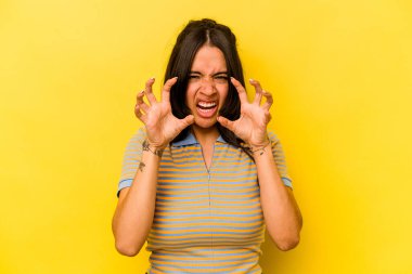 Sarı arka planda izole edilmiş genç İspanyol kadın pençelerini kedi taklidi yaparken gösteriyor, agresif bir hareket..