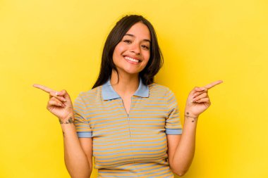 Sarı arka planda izole edilmiş genç İspanyol kadın farklı kopya alanlarını gösteriyor, birini seçiyor, parmaklarıyla gösteriyor.