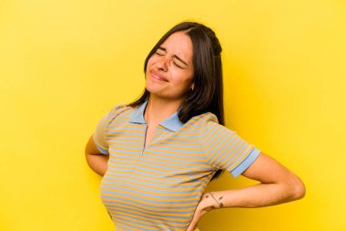 Sarı arka planda izole edilmiş sırt ağrısı çeken genç İspanyol kadın..