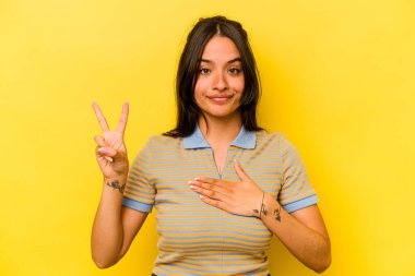 Sarı arka planda izole edilmiş genç İspanyol kadın yemin ediyor, elini göğsüne koyuyor..