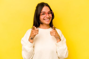 Sarı arka planda izole edilmiş genç İspanyol kadın parmaklarıyla ön tarafı işaret ediyor..
