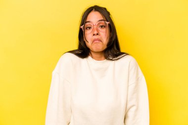 Sarı arka planda izole edilmiş genç İspanyol kadın omuzlarını silker ve gözleri açık kalır..