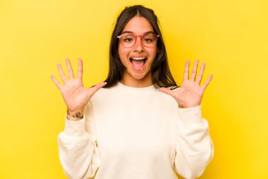Sarı arka planda izole edilmiş genç İspanyol kadın hoş bir sürprizle karşılaşıyor, heyecanlı ve el kaldırıyor..
