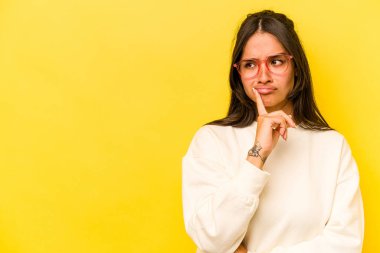 Sarı arka planda izole edilmiş genç İspanyol kadın şüpheli ve şüpheci bir ifadeyle yana bakıyor..