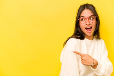 Sarı arka planda izole edilmiş genç İspanyol kadın başparmak uzakta, gülüyor ve kaygısız..