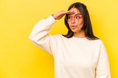 Sarı arka planda izole edilmiş genç İspanyol kadın uzaklara bakıyor ve elini alnına koyuyor..