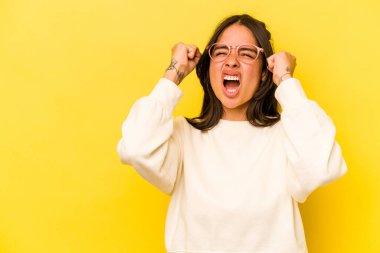 Sarı arka planda izole edilmiş genç İspanyol kadın zaferden sonra yumruk kaldırıyor, kazanan konsept..