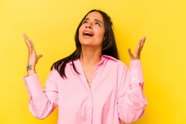 Sarı arka planda izole edilmiş genç İspanyol kadın gökyüzüne haykırıyor, yukarı bakıyor, hayal kırıklığına uğramış..