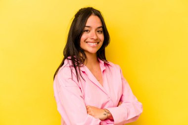 Sarı arka planda izole edilmiş, kendinden emin, kararlılıkla kollarını kavuşturan genç İspanyol kadın..