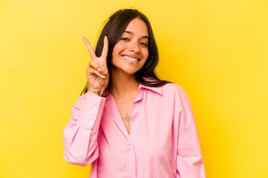 Sarı arka planda izole edilmiş genç İspanyol kadın iki numarayı parmaklarıyla gösteriyor..