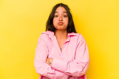 Sarı arka planda izole edilmiş genç İspanyol kadın yanakları patlatıyor, yorgun bir ifadesi var. Yüz ifadesi kavramı.