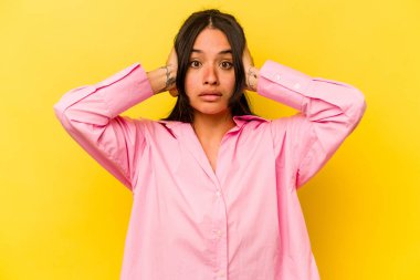 Sarı arka planda izole edilmiş genç İspanyol kadın kulaklarını elleriyle kapatıyor ve çok fazla ses duymamaya çalışıyor..