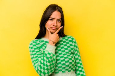 Latin kökenli genç bir kadın, sarı arka planda izole edilmiş. Bir strateji planlıyor, bir iş yolu düşünüyor..