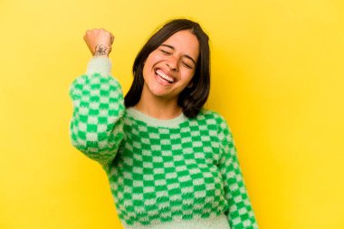 Sarı arka planda izole edilmiş genç İspanyol kadın zaferi, tutkuyu ve coşkuyu kutluyor, mutlu bir ifade..