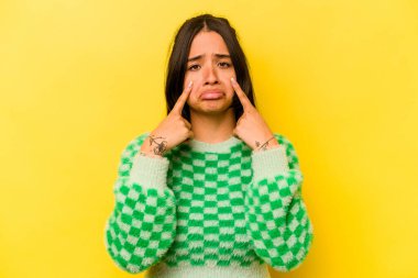 Sarı arka planda izole edilmiş genç İspanyol kadın ağlıyor, bir şeyden memnun değil, acı ve kafa karışıklığı konsepti..