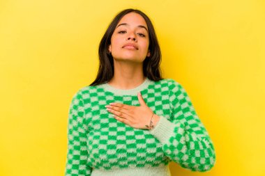 Sarı arka planda izole edilmiş genç İspanyol kadın yemin ediyor, elini göğsüne koyuyor..