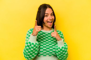Sarı arka planda izole edilmiş genç İspanyol kadın parmaklarıyla ön tarafı işaret ediyor..