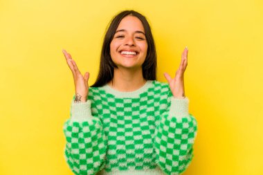 Sarı arka planda izole edilmiş genç İspanyol kadın yüksek sesle gülüyor elini göğsüne koyuyor..