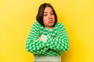 Sarı arka planda izole edilmiş genç İspanyol kadın omuzlarını silker ve gözleri açık kalır..