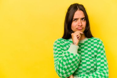 Sarı arka planda izole edilmiş genç İspanyol kadın şüpheli ve şüpheci bir ifadeyle yana bakıyor..