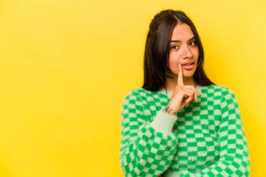 Sarı arka planda izole edilmiş genç İspanyol kadın şüpheli ve şüpheci bir ifadeyle yana bakıyor..