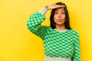 Sarı arka planda izole edilmiş genç İspanyol kadın uzaklara bakıyor ve elini alnına koyuyor..