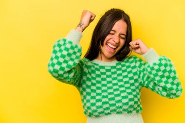 Sarı arka planda izole edilmiş genç İspanyol kadın zaferden sonra yumruk kaldırıyor, kazanan konsept..