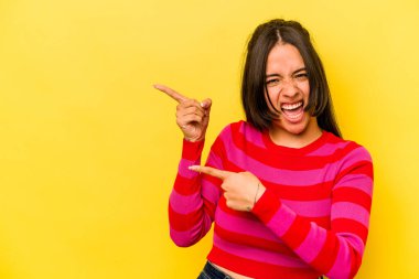 Sarı arka planda izole edilmiş genç İspanyol kadın işaret parmaklarıyla fotokopi alanını işaret ederek heyecan ve arzusunu ifade ediyor..
