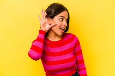 Sarı arka planda izole edilmiş genç İspanyol kadın bir dedikoduyu dinlemeye çalışıyor..