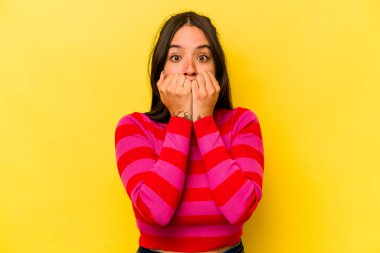 Sarı arka planda izole edilmiş, tırnak yiyen, gergin ve endişeli genç bir kadın..