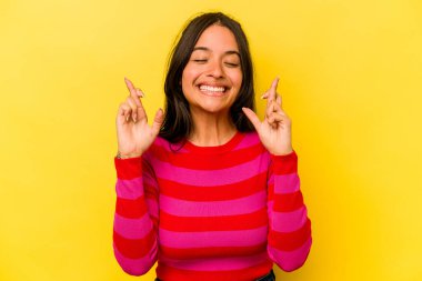 Sarı arka planda izole edilmiş genç İspanyol kadın şans diliyor.