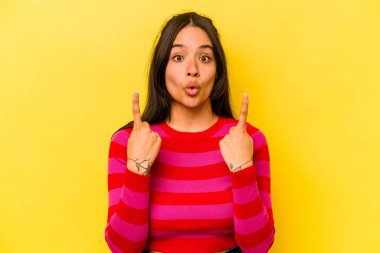 Sarı arka planda izole edilmiş, ağzı açık, üst tarafı işaret eden genç İspanyol kadın..