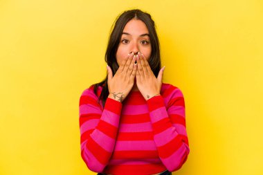 Sarı arka planda izole edilmiş genç İspanyol kadın elleriyle ağzını kapatırken şok oldu..