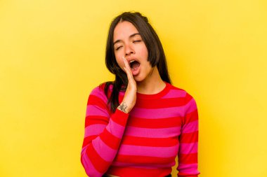 Sarı arka planda izole edilmiş genç İspanyol kadın esniyor. Ağzı eliyle kapatan yorgun bir hareket sergiliyor..