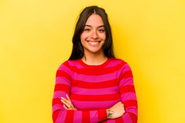 Sarı arka planda izole edilmiş, kendinden emin, kararlılıkla kollarını kavuşturan genç İspanyol kadın..