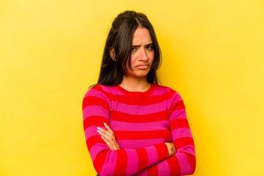 Sarı arka planda izole edilmiş genç İspanyol kadın şüpheli, belirsiz, seni muayene ediyor..