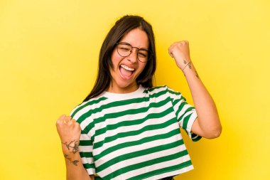 Sarı arka planda izole edilmiş genç İspanyol kadın tasasız ve heyecanlı bir şekilde tezahürat yapıyor. Zafer konsepti.