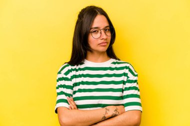 Sarı arka planda izole edilmiş genç İspanyol kadın alaycı bir ifadeyle kameraya bakıyor..