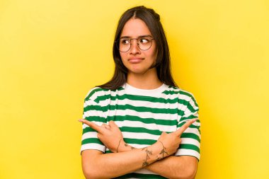 Sarı arka plan noktalarında izole edilmiş genç İspanyol kadın iki seçenek arasında seçim yapmaya çalışıyor..