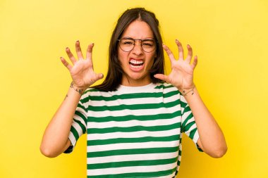 Sarı arka planda izole edilmiş genç İspanyol kadın pençelerini kedi taklidi yaparken gösteriyor, agresif bir hareket..