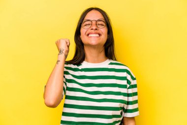 Sarı arka planda izole edilmiş genç İspanyol kadın zaferi, tutkuyu ve coşkuyu kutluyor, mutlu bir ifade..