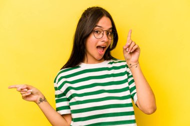 Sarı arka planda izole edilmiş genç İspanyol kadın farklı kopya alanlarını gösteriyor, birini seçiyor, parmaklarıyla gösteriyor.