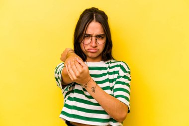 Sarı arka planda izole edilmiş genç İspanyol kadın stresten dolayı boynu ağrıyor, masaj yapıyor ve elle dokunuyor..