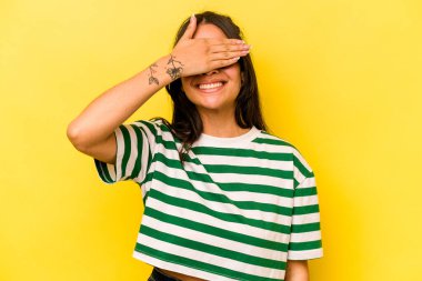 Sarı arka planda izole edilmiş genç İspanyol kadın elleriyle gözlerini kapatıyor, geniş bir gülümsemeyle bir sürpriz bekliyor..