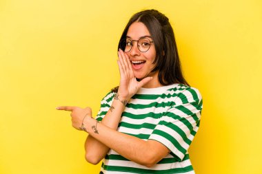 Latin kökenli genç bir kadın sarı arka planda izole edilmiş. Dedikodu yapıyor, bir şeyleri bildiriyor..